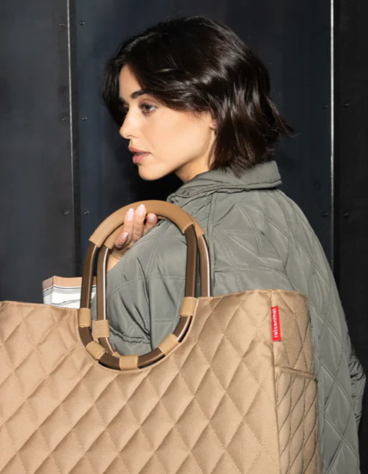 Frau mit kurzem dunklem Haar trägt gesteppte hellbraune Shopper-Tasche an Schulter