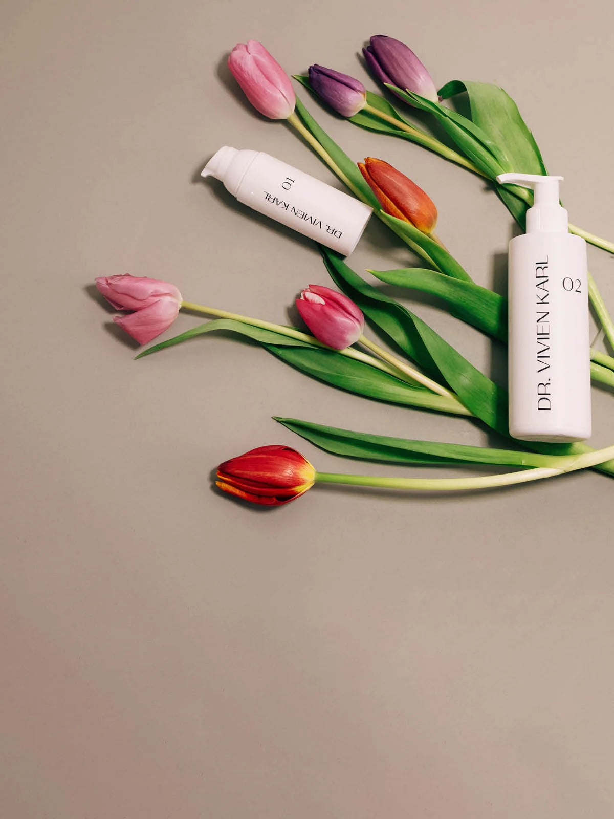 weiße Dr Vivien Karl Flaschen neben violetten roten Tulpen auf beigem Untergrund
