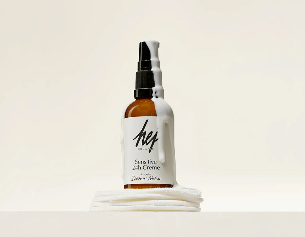 Braune Pumpflasche Hej Organic Sensitive 24h Creme mit tropfender weißer Creme auf weißen Tüchern