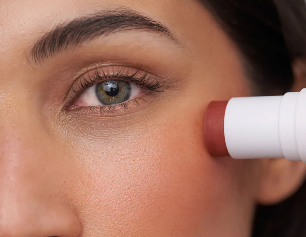 Nahaufnahme grünes Auge und weißer Cremeblushstick auf rosiger Wange