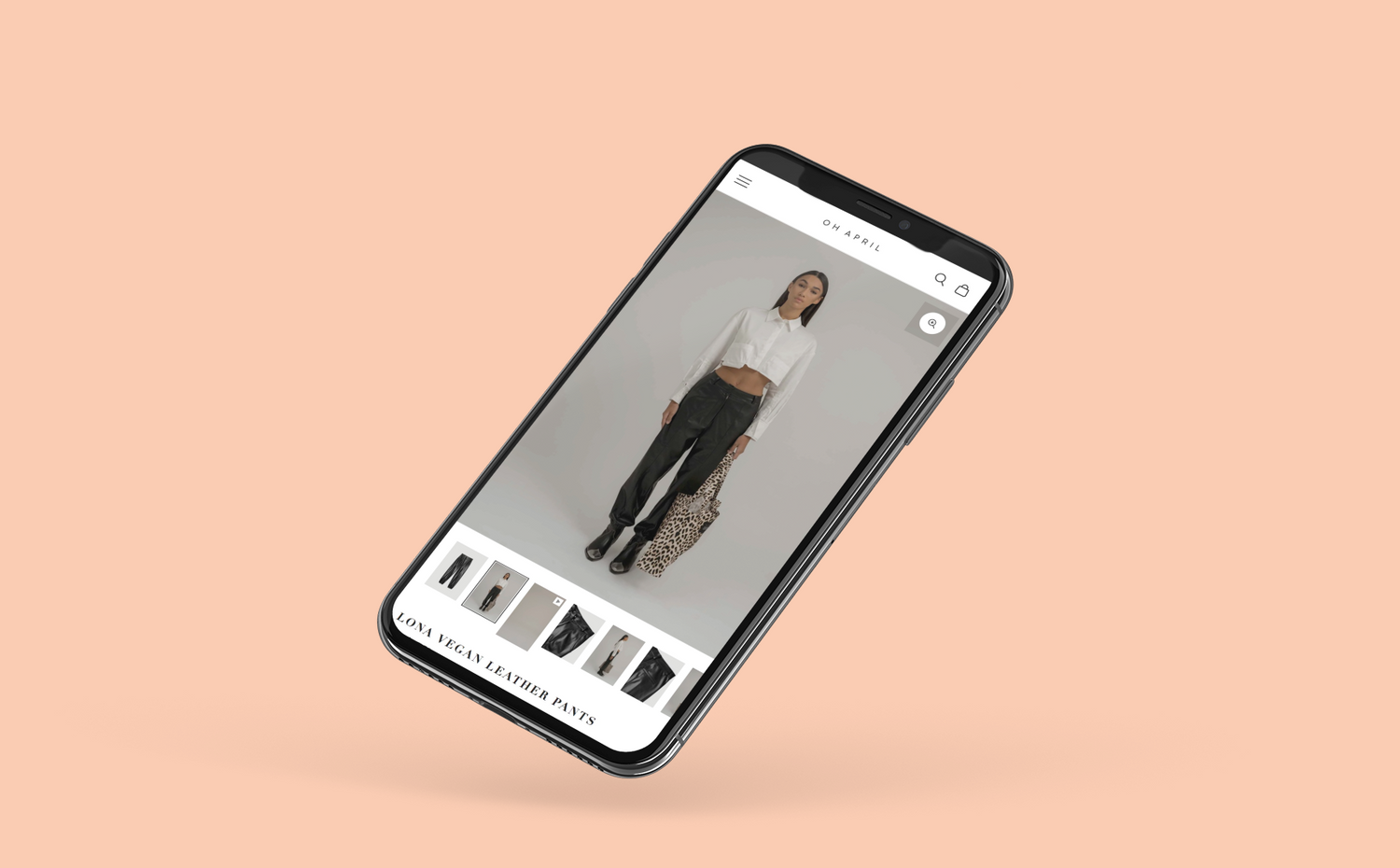 Schwebendes Smartphone-Display zeigt Model in weißer Cropped-Bluse, veganen Lederhosen und Leopardenmuster-Tasche vor pfirsichfarbenem Hintergrund