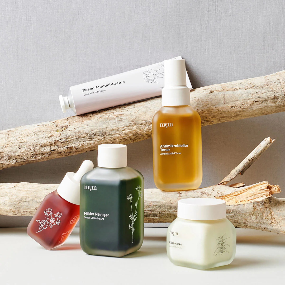 Kosmetikprodukte auf Treibholz helle Tube Rosen-Mandel-Creme bernsteinfarbener antimikrobieller Toner grünes Reinigungsöl rotes Serum milchweiße CBD-Maske