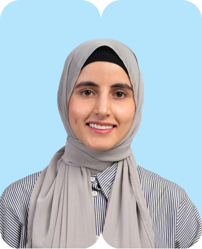 Lächelnde Frau mit grauem Hijab und gestreiftem Hemd vor pastellblauem Hintergrund