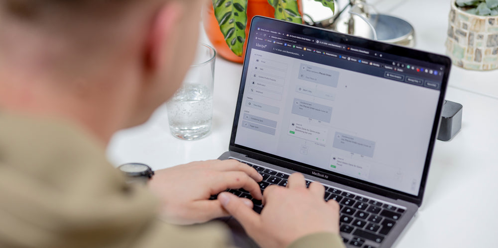 Person tippt Klaviyo Automatisierungs-Workflow auf MacBook Air neben Glas Wasser und Topfpflanzen